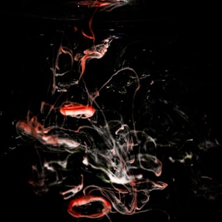 Swirling patterns of red and white smoke or liquid move through a dark background, creating an abstract and ethereal effect. The red shapes are reminiscent of pill capsules, and the white fluid creates a misty, ghost-like appearance.