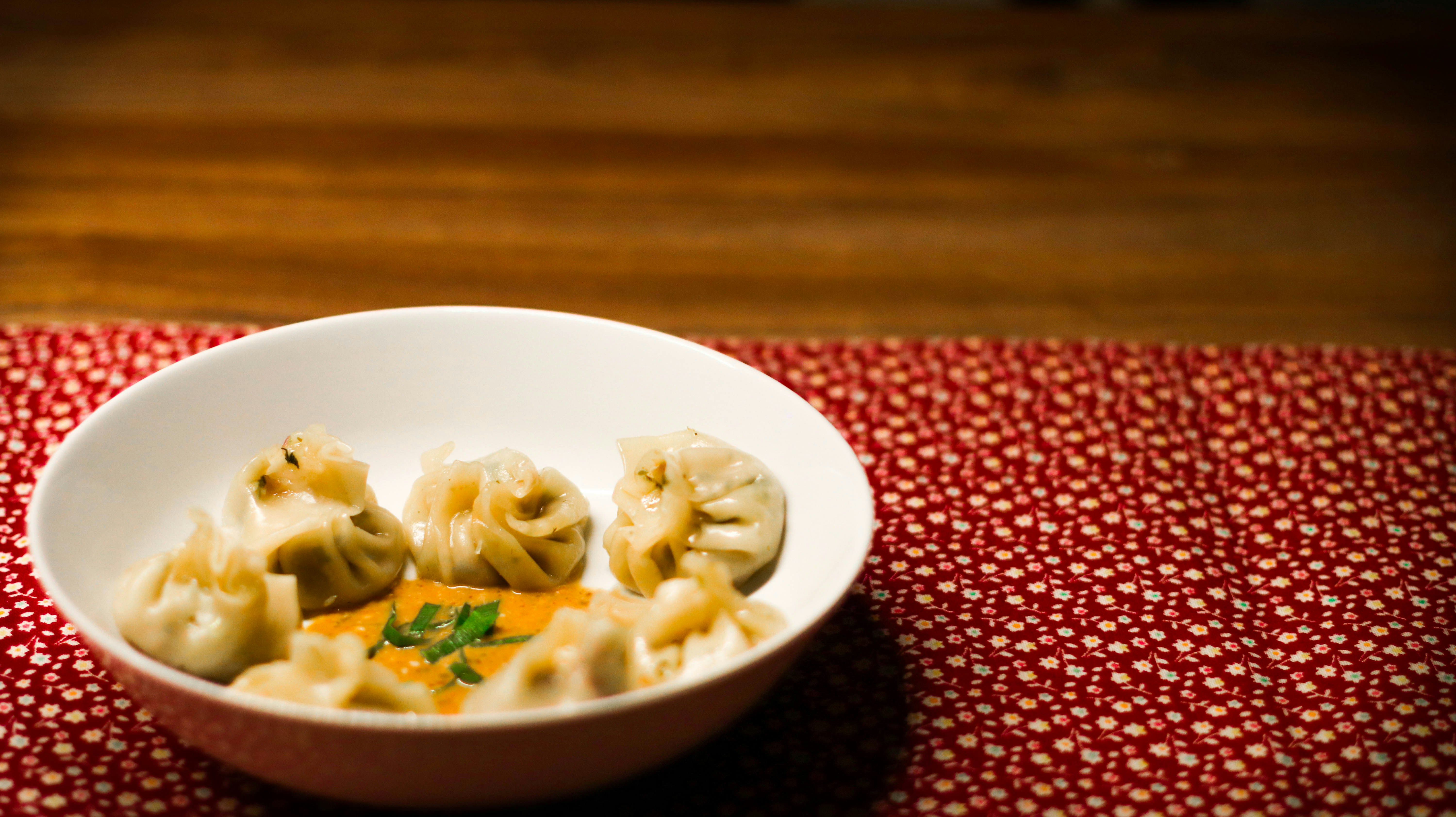 Steamed dumplings with red chili sauce and fresh herbs on wooden board