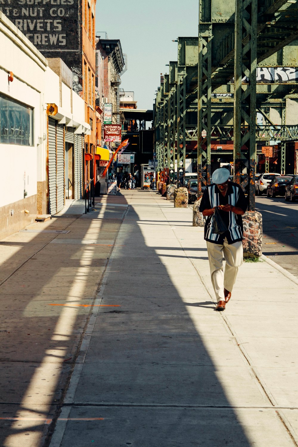 woman in black jacket and white pants walking on sidewalk during daytime