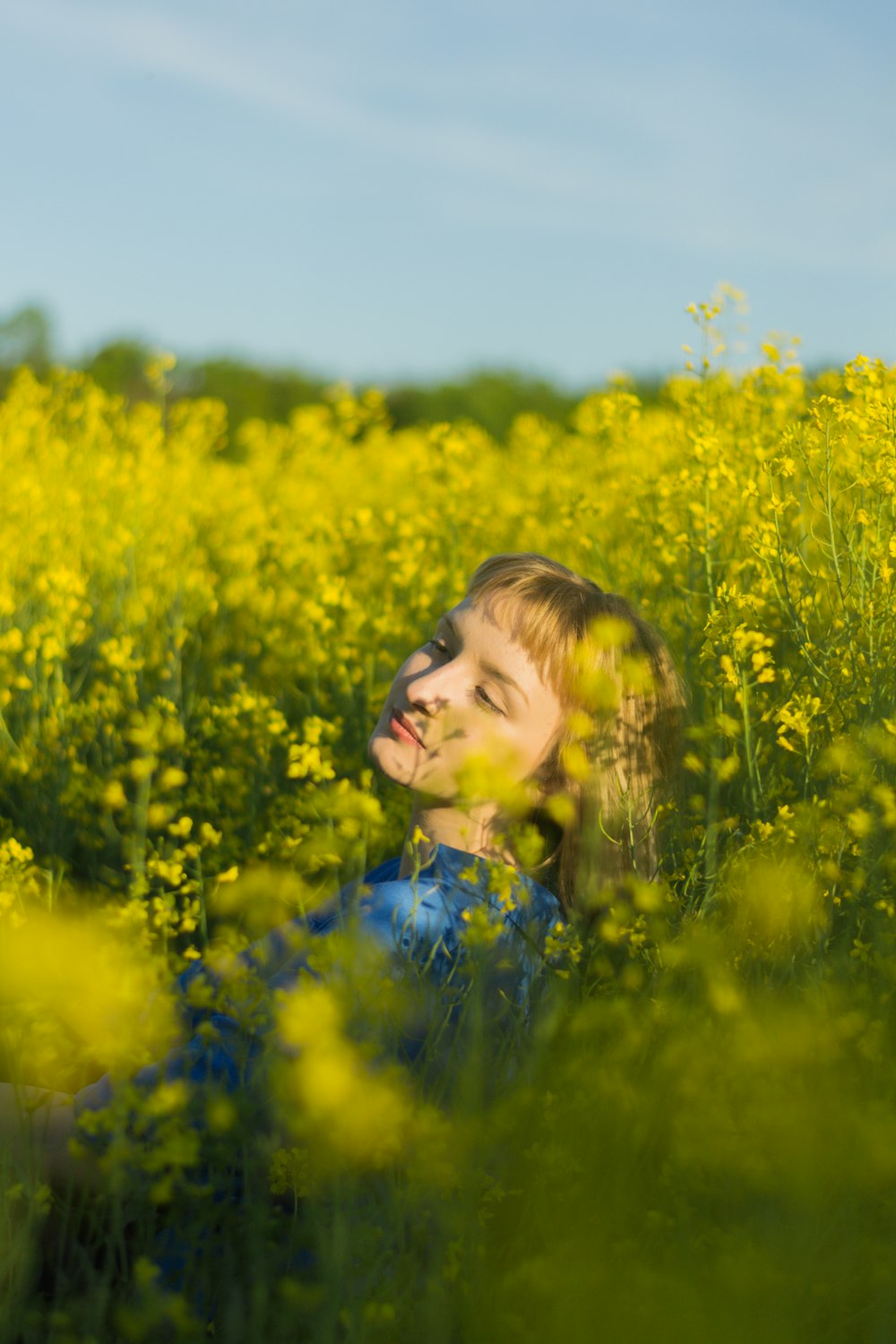 Muchacha en vestido floral azul de pie en el campo de flores amarillas durante el día