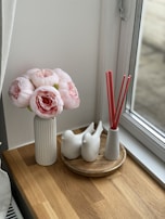 Close-up of a delicate floral reed diffuser surrounded by fresh blossoms on a sunlit windowsill.