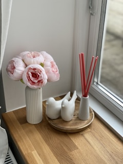 Close-up of a delicate floral reed diffuser surrounded by fresh blossoms on a sunlit windowsill.
