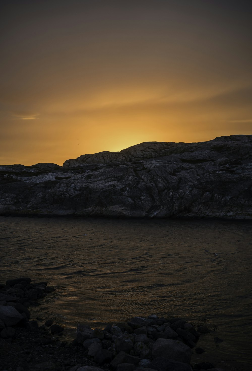 brown rocky mountain beside body of water during sunset