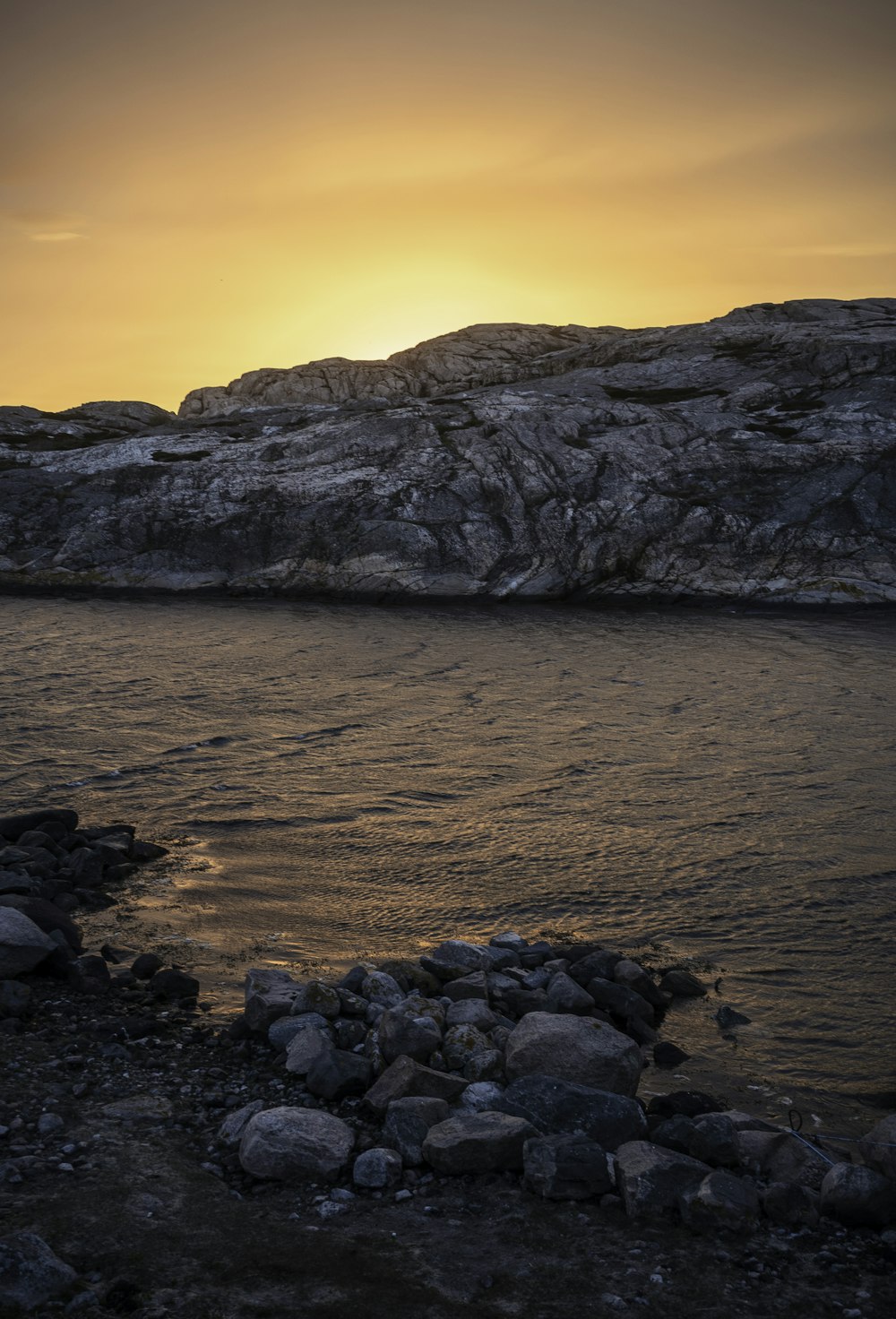 Montaña rocosa marrón al lado del cuerpo de agua durante la puesta del sol