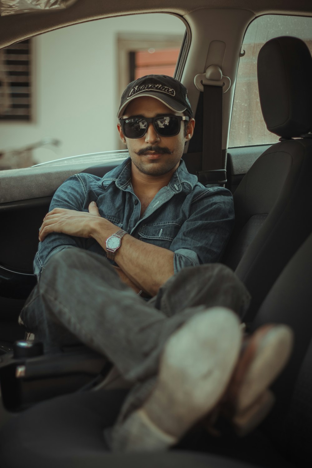 man in blue denim button up jacket wearing black sunglasses sitting on car seat