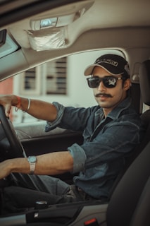 man in blue denim jacket wearing black sunglasses driving car during daytime