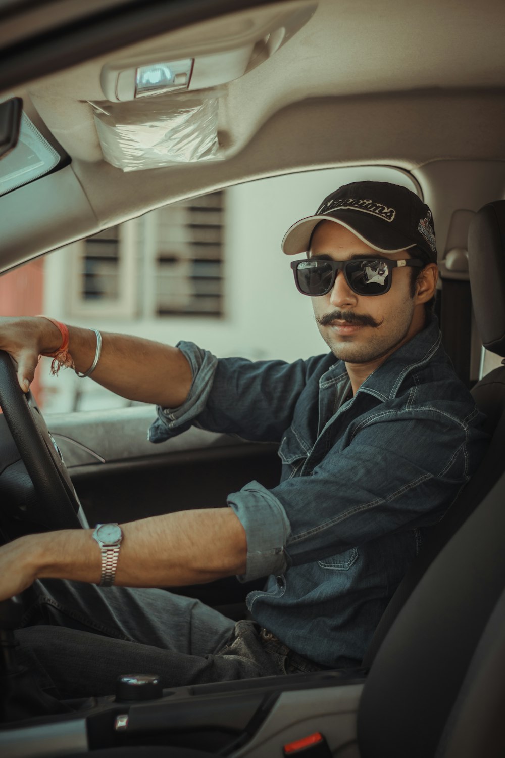 man in blue denim jacket wearing black sunglasses driving car during daytime
