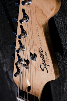 A close-up view of the headstock of a Fender Squier Bullet Strat electric guitar, showcasing its tuning pegs and brand logo against a dark background.
