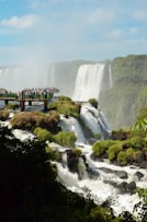 people standing on wooden bridge over waterfalls during daytime