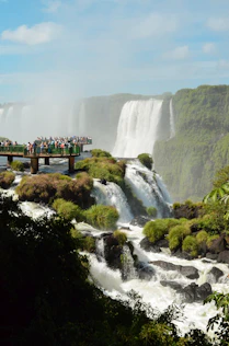 people standing on wooden bridge over waterfalls during daytime