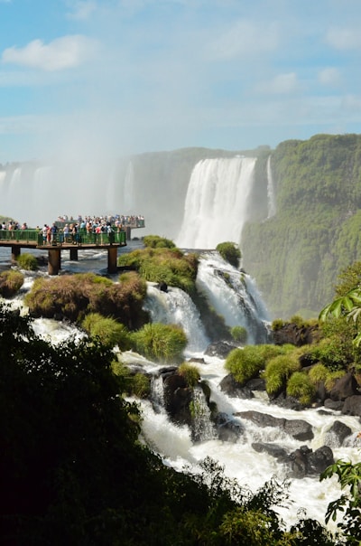 people standing on wooden bridge over waterfalls during daytime