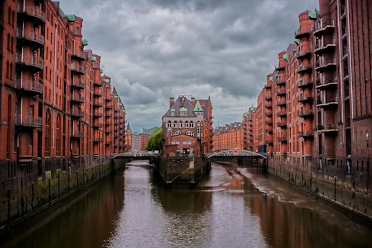 brown concrete building beside river during daytime in Speicherstadt Germany