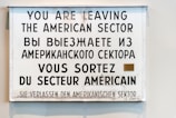 A multilingual sign displaying a warning in four languages: English, Russian, French, and German. It announces the departure from the American sector, indicating historical significance.