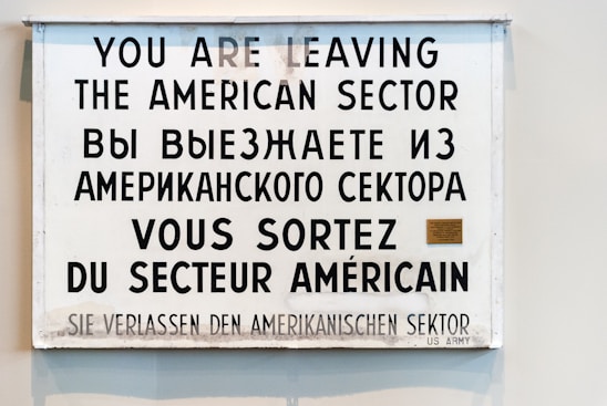 A multilingual sign displaying a warning in four languages: English, Russian, French, and German. It announces the departure from the American sector, indicating historical significance.