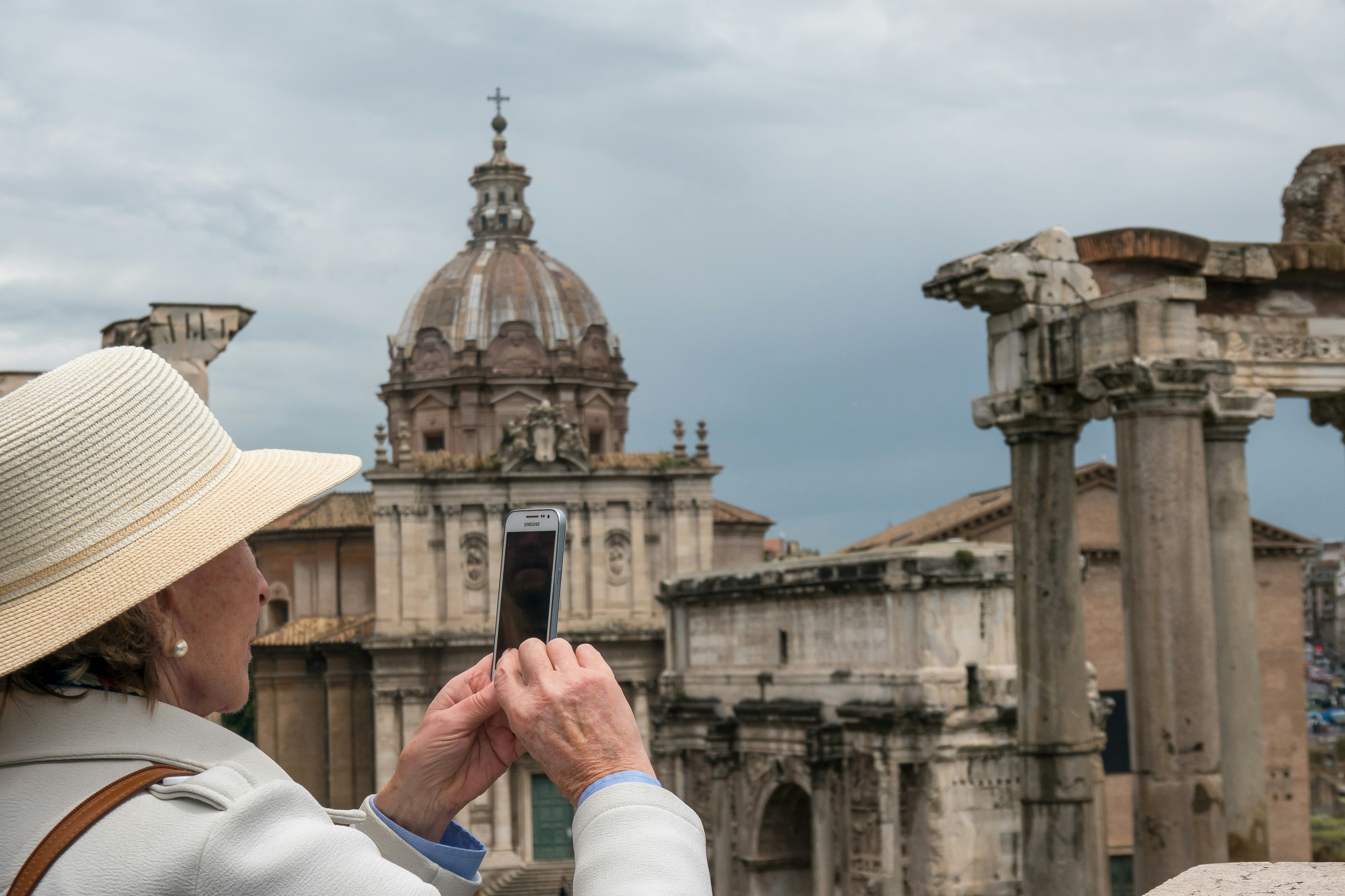 man in white long sleeve shirt holding smartphone, woman taking picture on vacation in rome