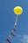 A large yellow balloon is floating in the sky, tethered by a string adorned with alternating red and yellow triangular flags. The sky is clear with a few wispy clouds.