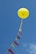 A large yellow balloon is floating in the sky, tethered by a string adorned with alternating red and yellow triangular flags. The sky is clear with a few wispy clouds.