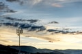 A telecommunications tower stands prominently against a backdrop of rolling hills and a dramatic sky filled with clouds. The sunlight casts a warm glow, creating a soothing yet dynamic contrast.