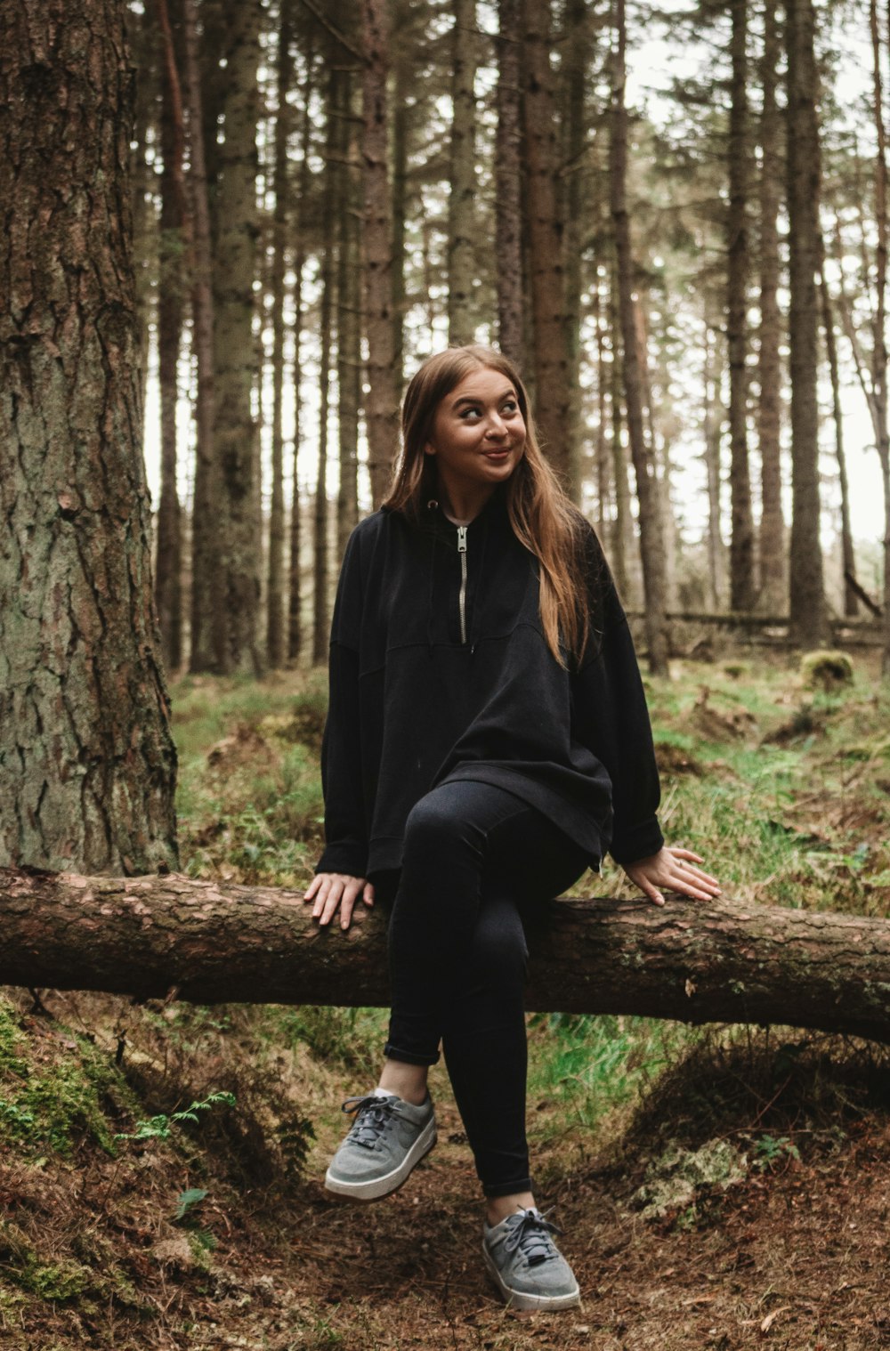 茶色の木の幹に座っている黒い長袖シャツの女性