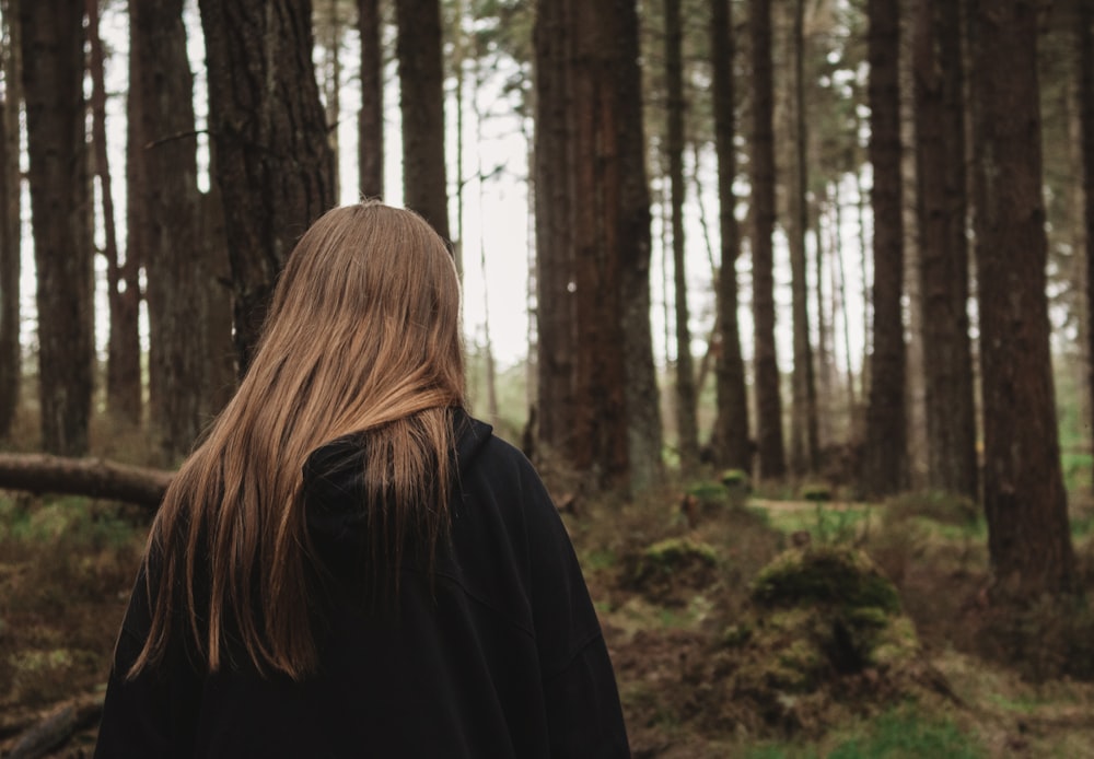 woman in black jacket standing in forest during daytime