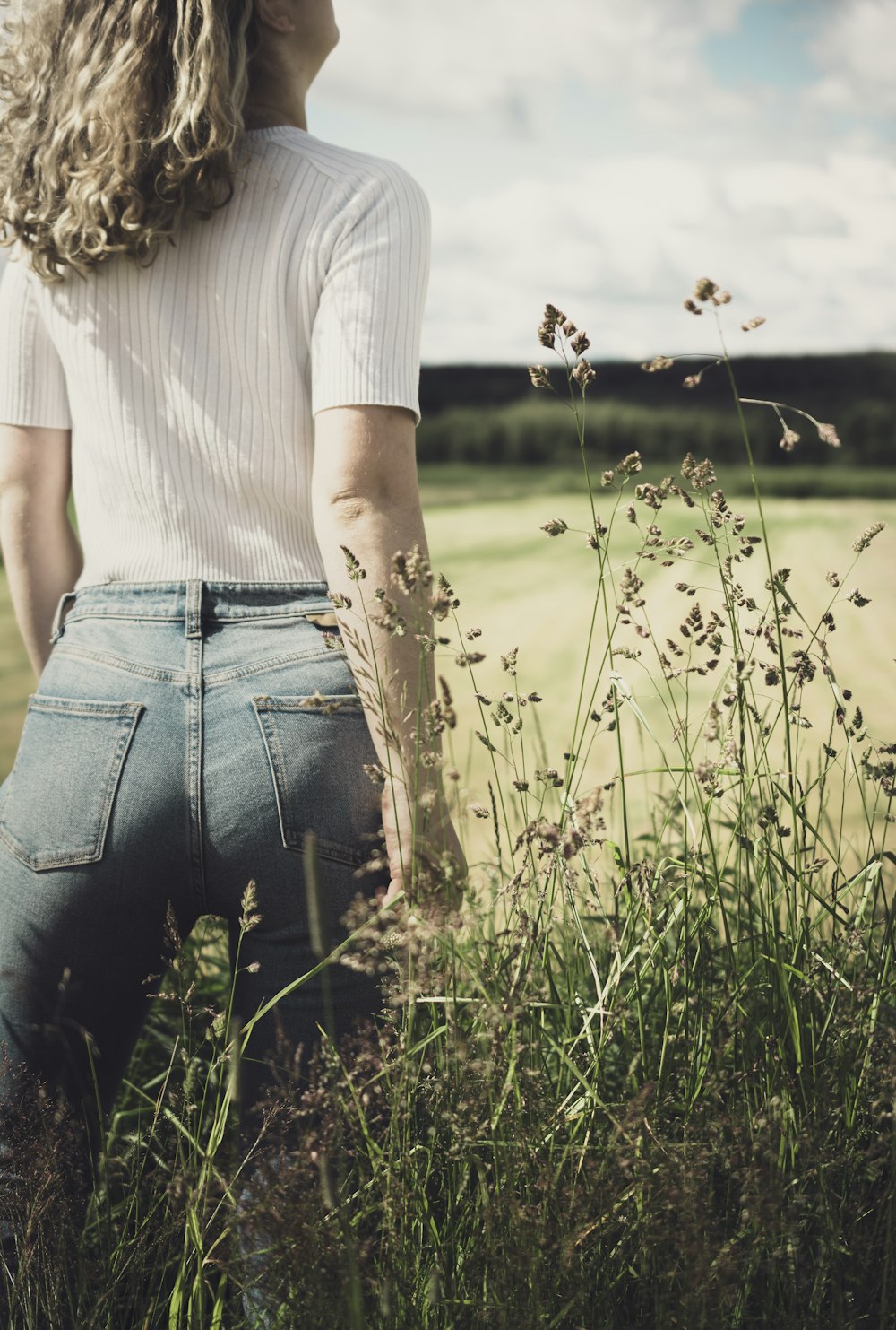 Donna in camicia bianca e jeans blu in denim in piedi sul campo di erba verde durante il giorno