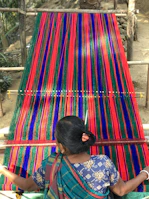 Artisan hands weaving a forest green linen saree on a traditional loom.