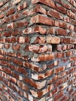 A close-up view of a brick wall corner, with roughly textured red bricks and visible gray mortar between them, creating a rugged and sturdy appearance.