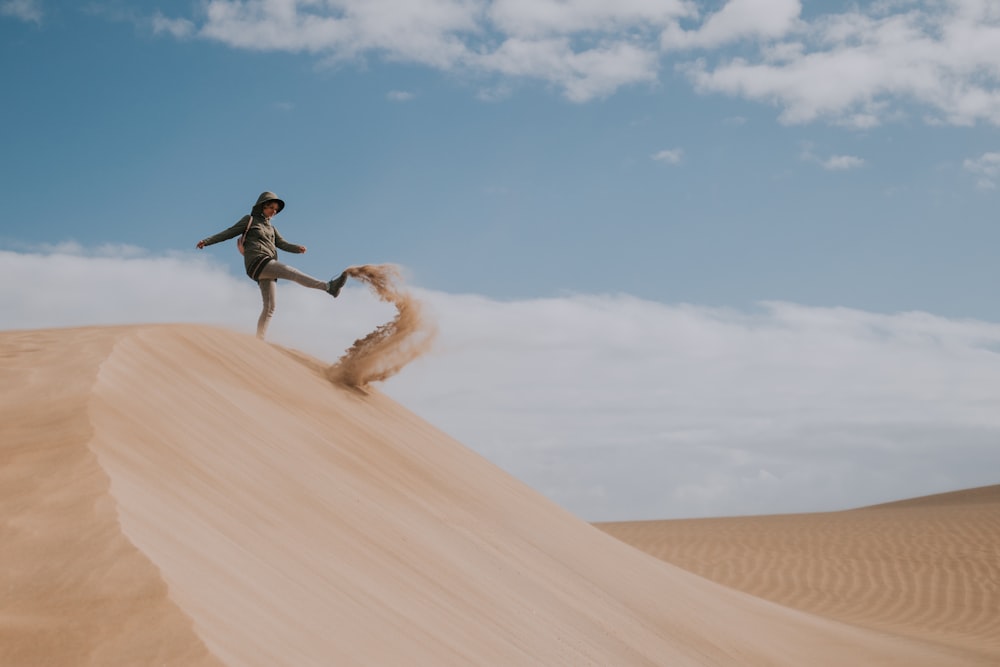 man in black jacket and pants jumping on brown sand during daytime