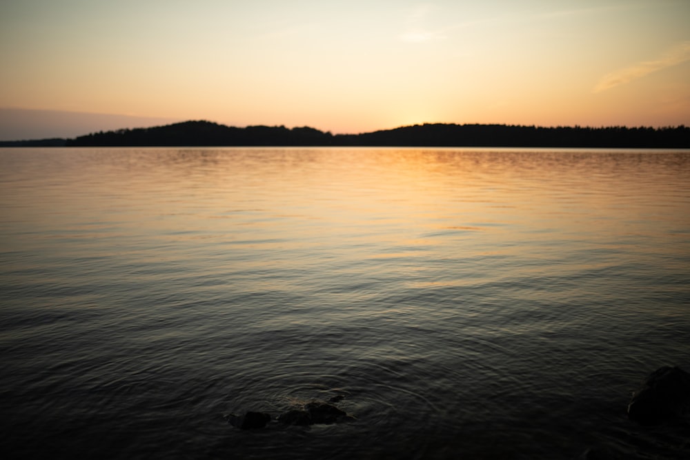 body of water near mountain during sunset