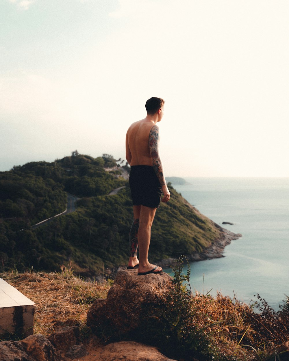 man in black shorts standing on brown rock near body of water during daytime