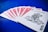 A set of playing cards spread out on a vibrant blue surface, highlighting a joker at the forefront. The backs of the other cards feature a red intricate design with white borders.