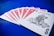 A set of playing cards spread out on a vibrant blue surface, highlighting a joker at the forefront. The backs of the other cards feature a red intricate design with white borders.