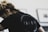 A person with light brown hair tied back is wearing a black shirt with the word 'INNER' printed on it in large letters. The focus is on the shirt, and the background is blurred, showing what appears to be framed pictures on a wall.