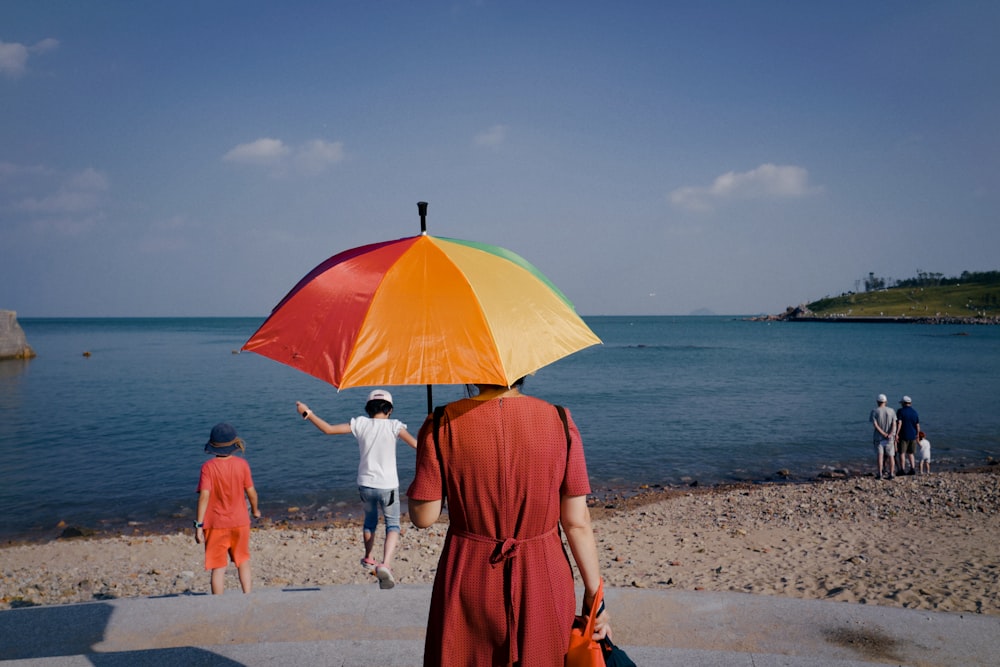 낮 동안 해변에서 우산을 들고 주황색 드레스를 입은 여자