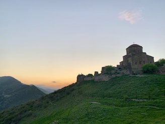 A peaceful stone church nestled among rolling green hills under a soft blue sky.