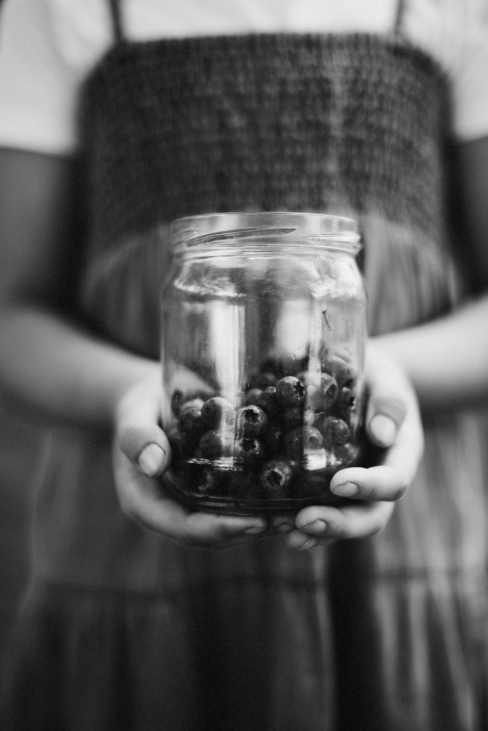 grayscale photo of person holding jar with black beads