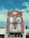 A historic red brick building with intricate architectural details, including pointed spires and arched windows. A 'For Lease' sign is prominently displayed on the building's facade. The sky is a bright blue with scattered clouds, providing a vivid background.