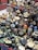 A collection of various antiques and brass ornaments displayed on a patterned cloth. The assortment includes intricate figurines, brass cups, a large key, padlocks, an hourglass, and decorative items like painted nesting dolls.