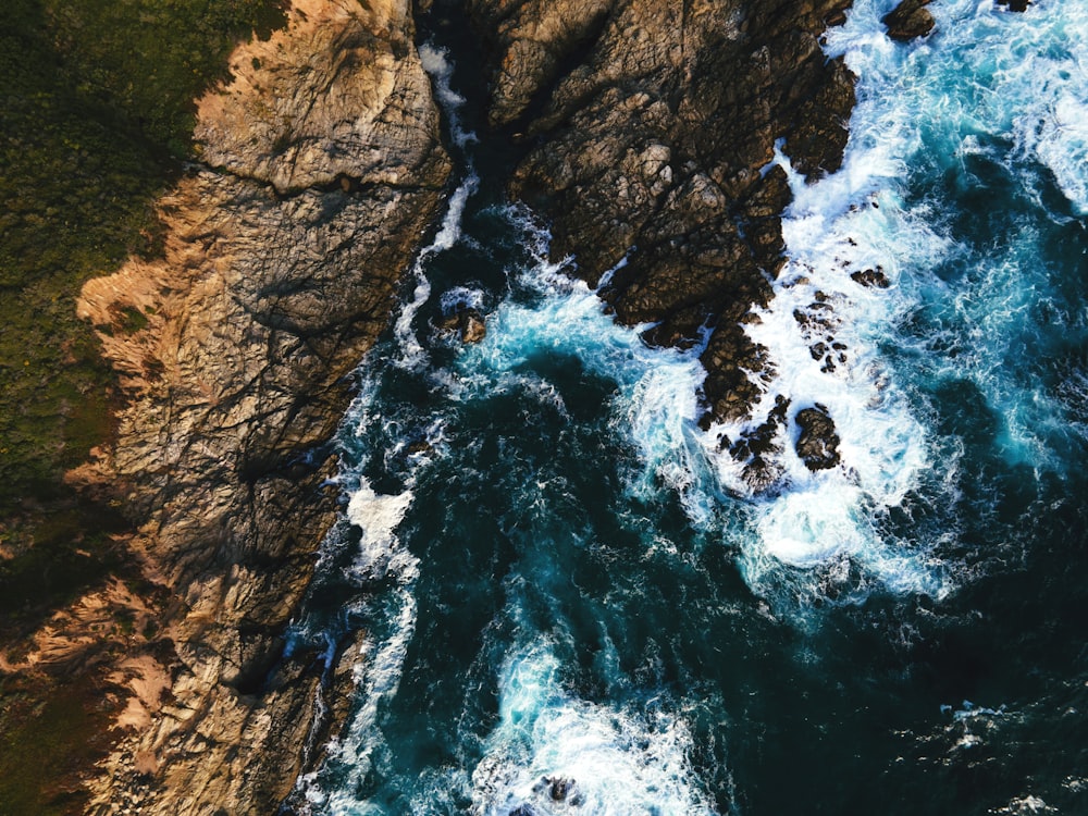 water waves hitting brown rocky mountain during daytime