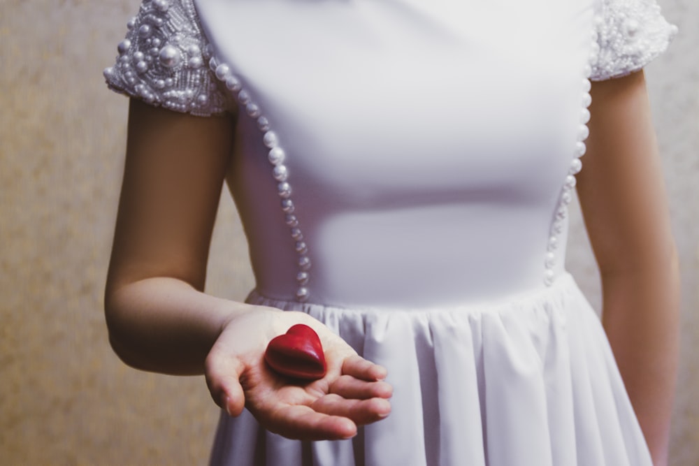 woman in white sleeveless dress holding red round fruit
