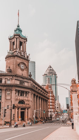 A city street features historic and modern architecture, with a prominent clock tower building adorned with a flag. The street is bustling with vehicles and pedestrians, and tall skyscrapers are visible in the background.