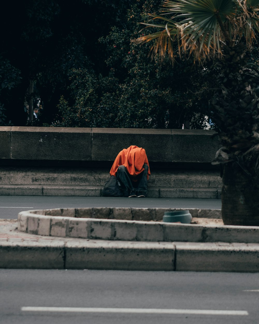 man in orange hoodie sitting on gray concrete stairs