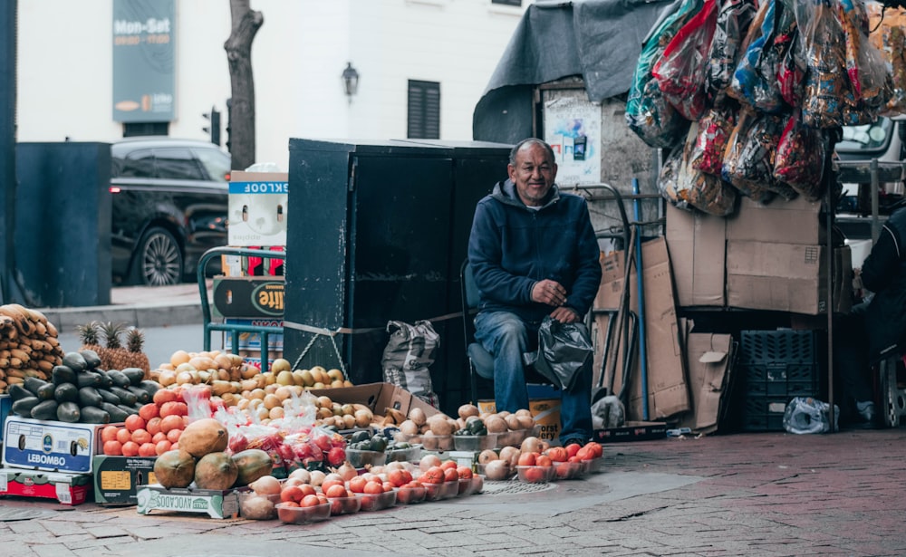uomo in giacca nera che si siede sul marciapiede di cemento grigio circondato da frutti rossi della mela durante il giorno
