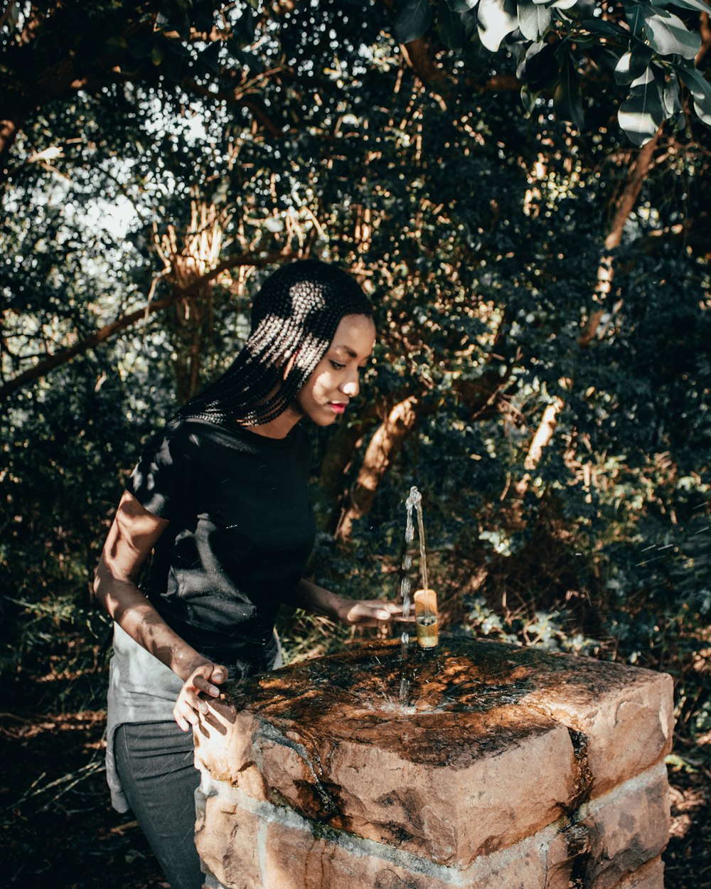 man in black t-shirt and blue denim jeans sitting on brown rock