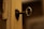 An old, rusty key inserted into a lock on a worn wooden door. The door's paint is chipped and the hardware surrounding the keyhole has a vintage appearance. The background is blurred, focusing attention on the key and lock.
