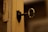 An old, rusty key inserted into a lock on a worn wooden door. The door's paint is chipped and the hardware surrounding the keyhole has a vintage appearance. The background is blurred, focusing attention on the key and lock.