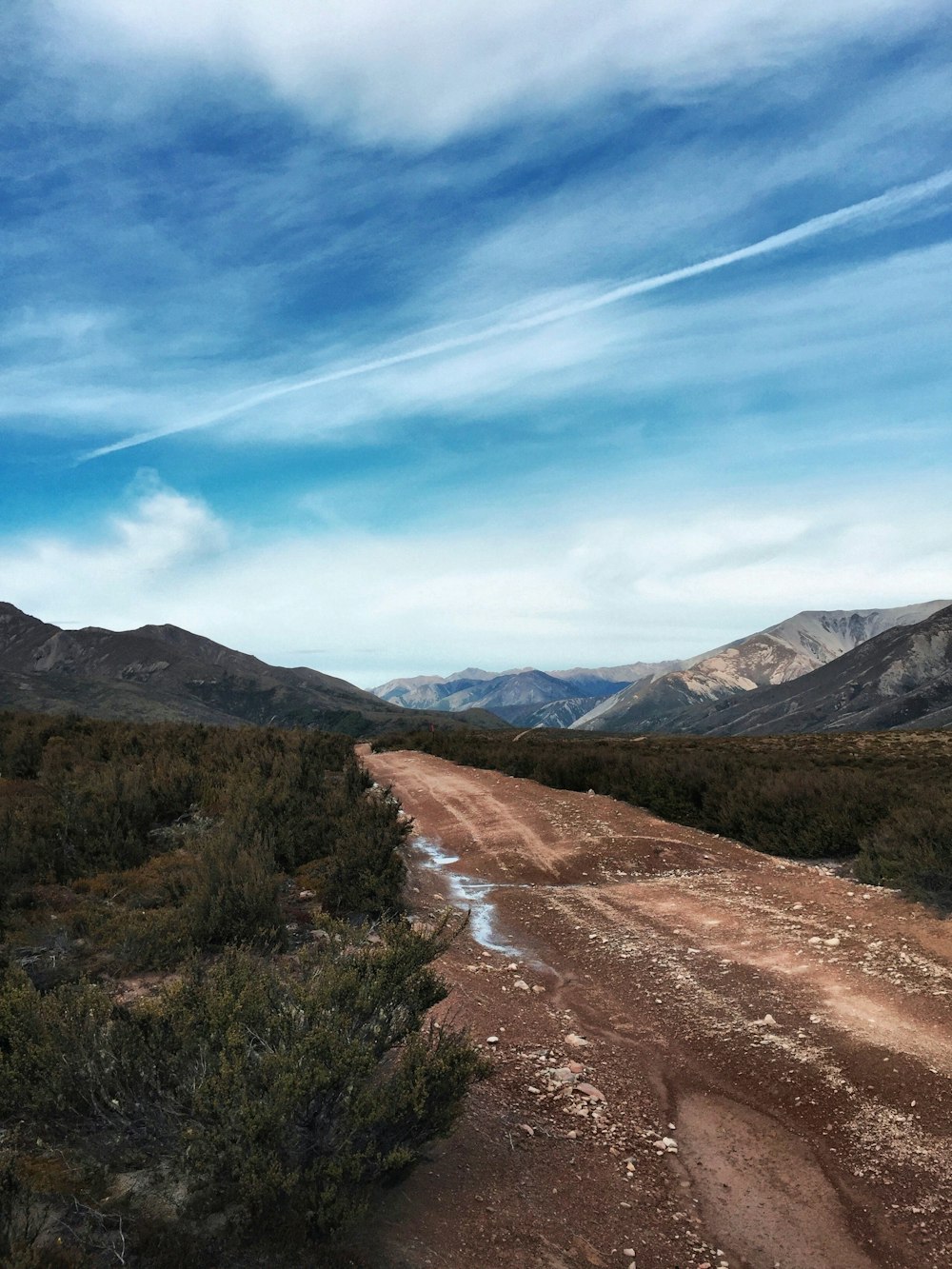 brown dirt road between green grass field under blue sky during daytime