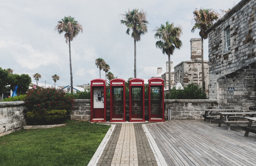 Cabina telefónica roja en el campo de hierba verde cerca del edificio de hormigón marrón durante el día