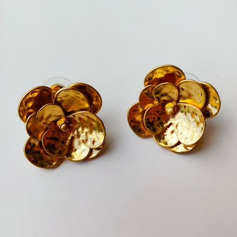 A pair of gold earrings with intricate patterns displayed against a soft background.