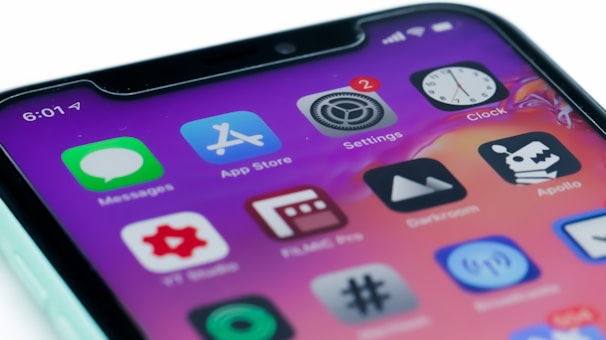 A close-up view of a smartphone screen displaying various app icons on a gradient background. The icons include Messages, App Store, Settings with a notification badge, and Clock, among others.